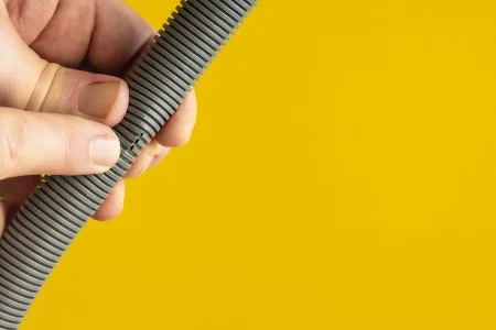 Hände halten einen grauen Schlauch vor gelbem Hintergrund.